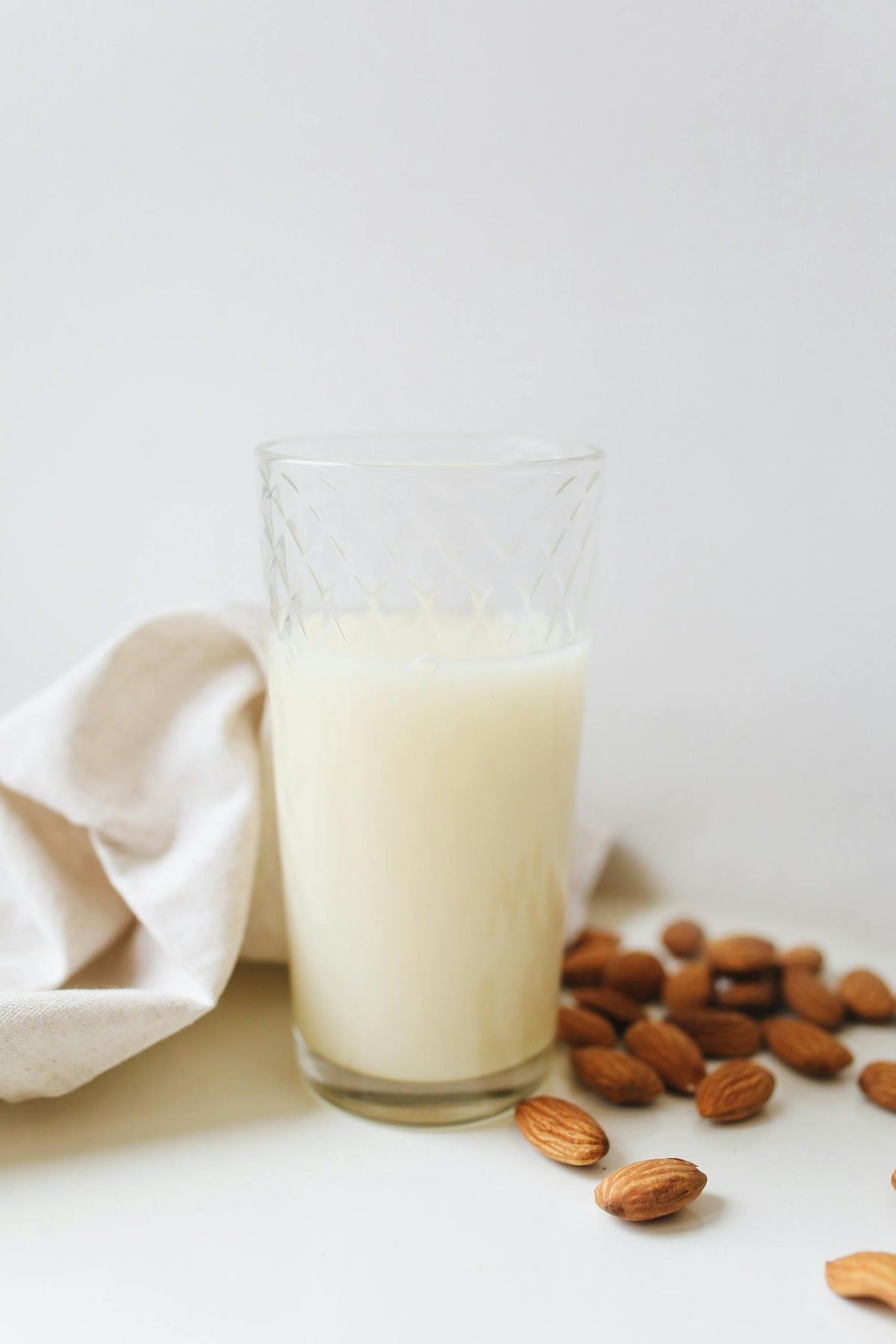 Glass of homemade almond milk surrounded by almonds